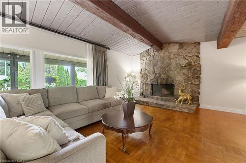 Stone fireplace feature with hearth, wood-finish parquet flooring, exposed wood ceiling beams, and expansive windows - 1316 Nevarc Drive, Burlington, ON 