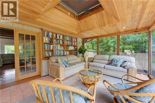 Wood-paneled ceiling with skylight, extensive built-in shelving, full-height window wall, French doors, and tile flooring - 1316 Nevarc Drive, Burlington, ON 