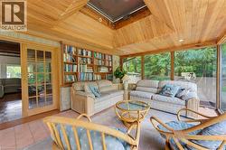 Wood-paneled ceiling with skylight, extensive built-in shelving, full-height window wall, French doors, and tile flooring - 