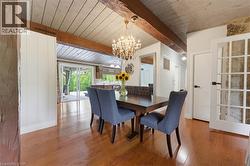 Wood-finish flooring, exposed wood beams, vaulted planked ceiling, sliding glass doors, and a chandelier with a metallic finish - 