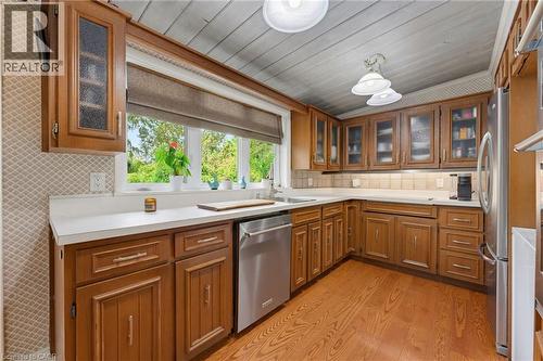 Wood-finish cabinetry with glass panel doors, white countertops, tile backsplash, and stainless steel appliances - 1316 Nevarc Drive, Burlington, ON 