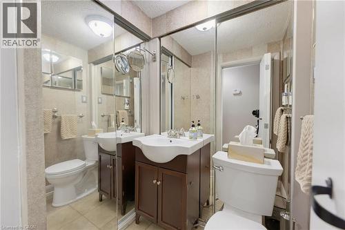 Bathroom featuring a white ceramic toilet, brown wood-finish vanity with an integrated sink, and full-wall mirrors - 1316 Nevarc Drive, Burlington, ON 