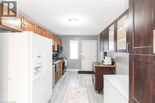 Wood-finish flooring, white paneled door, light-toned upper cabinetry, dark-toned cabinetry with glass inserts, and a stainless steel range - 42 Saturn Road, Port Colborne, ON 