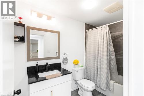 Bathroom with dark speckled countertop, white vanity, black faucet, framed mirror, and a tiled shower surround - 42 Saturn Road, Port Colborne, ON 