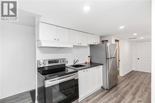 Kitchenette featuring white cabinetry, stainless steel appliances, dark countertop, and wood-finish flooring - 42 Saturn Road, Port Colborne, ON 