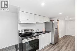 Kitchenette featuring white cabinetry, stainless steel appliances, dark countertop, and wood-finish flooring - 