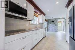 White cabinetry with granite countertops, stainless steel appliances, tile flooring, and a stone accent wall - 