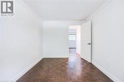 Wood-finish parquet flooring, white trim, white walls, and a white interior door with dark hardware - 