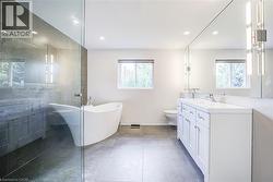 Freestanding soaking tub, frameless glass shower enclosure, double vanity with white cabinetry, integrated double sinks, and large wall-mounted mirror - 
