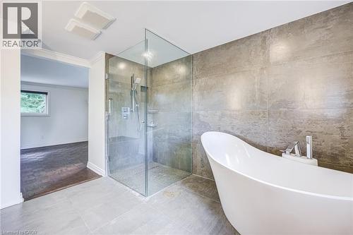 Expansive bathroom featuring a freestanding soaking tub, a walk-in shower with a glass enclosure, an integrated shower bench, and floor-to-ceiling wall tiling - 3148 Terraview Court, Burlington, ON 