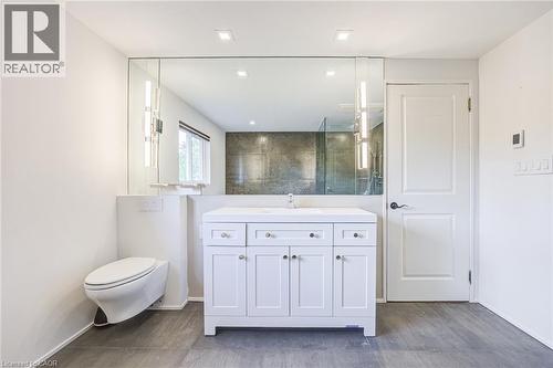 White shaker vanity with a single basin, wall-mounted floating toilet, and large rectangular mirror - 3148 Terraview Court, Burlington, ON 