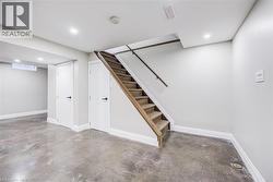 Concrete flooring, recessed lighting, white doors with matte black hardware, and wood-finish stairs with railing - 