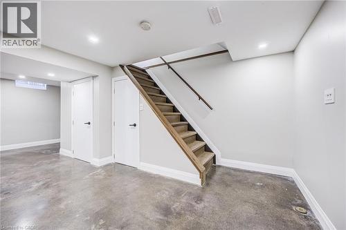 Concrete flooring, recessed lighting, white doors with matte black hardware, and wood-finish stairs with railing - 3148 Terraview Court, Burlington, ON 