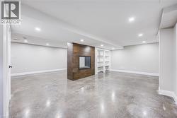 Spacious interior featuring concrete flooring, a fireplace with a wood-finish surround, built-in shelving, recessed lighting, and white baseboards - 