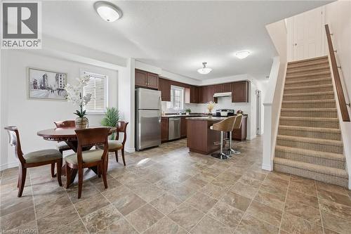 Open-concept living space with tiled flooring, a kitchen featuring dark wood cabinetry and stainless steel appliances, a kitchen island with seating, and a carpeted staircase - 931 Glasgow Street Unit# 27B, Kitchener, ON 