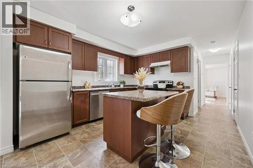 Full kitchen featuring wood-finish cabinetry, stainless steel appliances, stone-finish countertops, and a kitchen island with seating - 931 Glasgow Street Unit# 27B, Kitchener, ON 