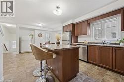 Kitchen featuring wood cabinetry, stainless steel appliances, a center island with seating, and tile flooring - 