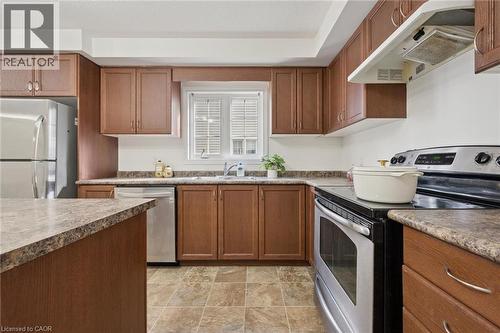 U-shaped kitchen with wood-finish cabinetry, tile flooring, stainless steel appliances, and a window with white louvered blinds - 931 Glasgow Street Unit# 27B, Kitchener, ON 