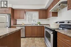 U-shaped kitchen with wood-finish cabinetry, tile flooring, stainless steel appliances, and a window with white louvered blinds - 