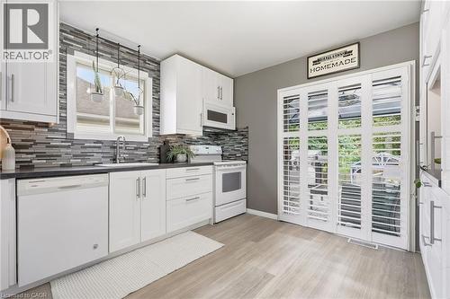 White cabinetry with brushed nickel hardware, dark countertops, a mosaic tile backsplash, wood-finish flooring, and white bi-fold doors - 94 Kent Road, Brantford, ON 