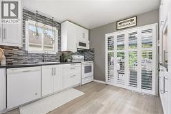 White cabinetry with brushed nickel hardware, dark countertops, a mosaic tile backsplash, wood-finish flooring, and white bi-fold doors - 
