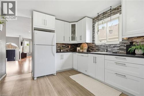Modern kitchen featuring white cabinetry, dark countertops, a mosaic tile backsplash, and light wood-finish flooring - 94 Kent Road, Brantford, ON 