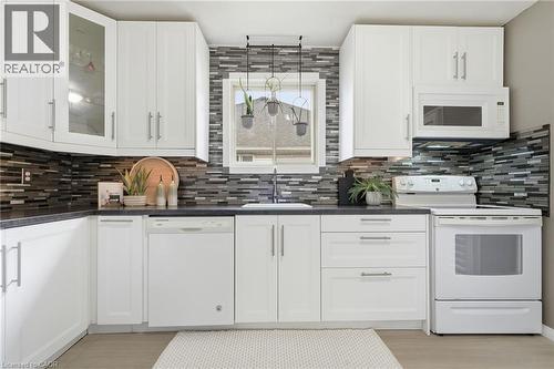 White cabinetry with silver-tone hardware, dark countertops, a mosaic tile backsplash, a built-in microwave, and a white range - 94 Kent Road, Brantford, ON 