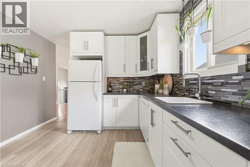 White cabinetry, dark countertops, a window over the sink, and wood-finish flooring - 94 Kent Road, Brantford, ON 