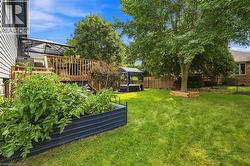 Expansive backyard featuring a manicured lawn, a raised garden bed, a wooden deck with a covered area, and mature trees - 