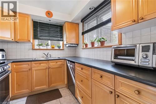 L-shaped kitchen with wood cabinetry, dark countertops, a double basin sink, and tile backsplash - 152 Hilda Avenue, North York, ON 
