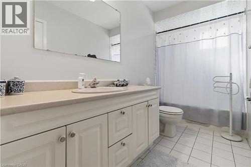 Bathroom featuring a white vanity with paneling, a neutral countertop, an integrated sink, a large wall-mounted mirror, and white square floor tiles - 152 Hilda Avenue, North York, ON 