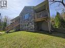 Exterior featuring an upper-level wooden deck with balustrade, a lower covered patio, and a stone-clad facade - 2516 Irish Line, Coldwater, ON 