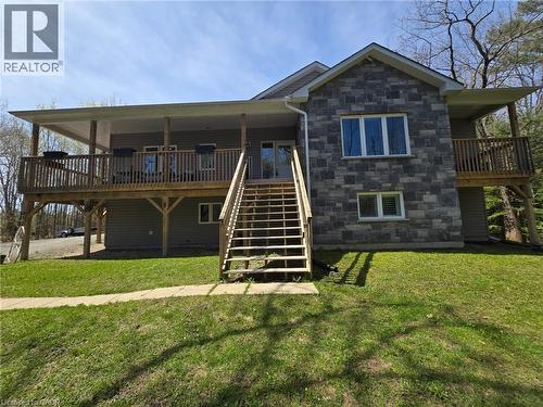 Modern residential exterior featuring stone-look and horizontal siding, a covered deck with wood railing, a secondary uncovered deck, and a multi-level wood staircase - 2516 Irish Line, Coldwater, ON 