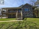 Modern residential exterior featuring stone-look and horizontal siding, a covered deck with wood railing, a secondary uncovered deck, and a multi-level wood staircase - 2516 Irish Line, Coldwater, ON 