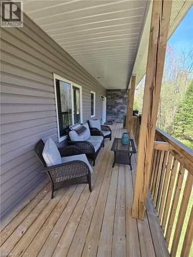 Expansive covered porch featuring a wood-plank floor, natural wood support posts, and a stone accent wall - 2516 Irish Line, Coldwater, ON 