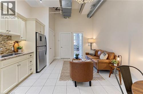 High ceilings with exposed ductwork, white tile flooring, cream cabinetry, a stainless steel refrigerator, and a mosaic tile backsplash - 25 Concession Street Unit# 110, Cambridge, ON 