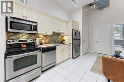 Kitchen featuring stainless steel appliances, upper and lower cabinetry, granite-style countertops, mosaic tile backsplash, and white tile flooring - 
