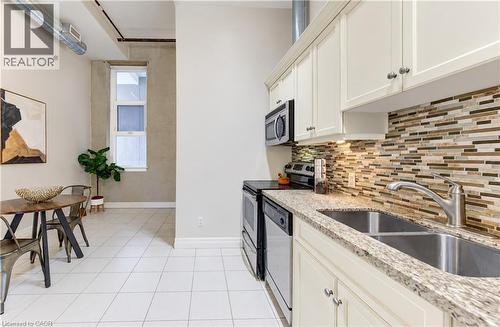 Kitchen featuring light cabinetry, stainless steel appliances, a double basin sink, and a mosaic tile backsplash - 25 Concession Street Unit# 110, Cambridge, ON 