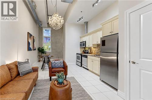 High ceilings with exposed ductwork, a multi-tiered crystal chandelier, white tile flooring, a kitchen with light-toned cabinetry, and stainless steel appliances - 25 Concession Street Unit# 110, Cambridge, ON 