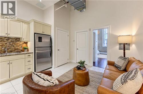 Kitchenette with cream cabinetry, stainless steel refrigerator, and tiled backsplash - 25 Concession Street Unit# 110, Cambridge, ON 