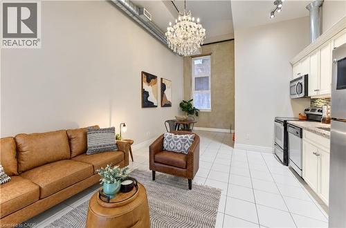 High ceilings with exposed ductwork, a multi-tiered crystal chandelier, white tile flooring, white shaker cabinets, and stainless steel appliances - 25 Concession Street Unit# 110, Cambridge, ON 