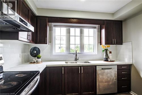 Dark wood-finish cabinetry, white subway tile backsplash, white countertops, stainless steel sink with a gooseneck faucet, and a large window with grid panes - 226 Maitland Street, Kitchener, ON 