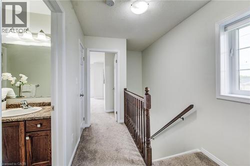 Carpeted hallway with a window, a wooden handrail, and a bathroom entry featuring a vanity with a sink - 226 Maitland Street, Kitchener, ON 
