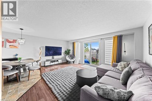Open-concept living area with wood-finish flooring, a sliding glass door to the backyard, and a dining area featuring a chandelier - 245 Red Clover Court, Kitchener, ON 