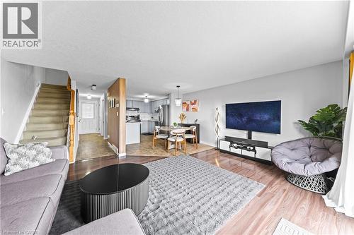 Open-concept living area with wood-finish flooring, a carpeted staircase, and an attached kitchen with light cabinetry - 245 Red Clover Court, Kitchener, ON 