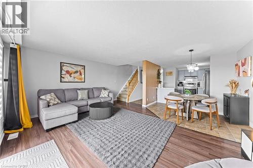 Wood-finish flooring, staircase with wood railings, kitchen with stainless steel appliances, and a dining area with pendant lighting - 245 Red Clover Court, Kitchener, ON 