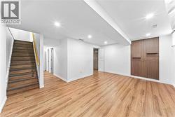 Recessed lighting, wood-finish flooring, wood slatted accent wall with integrated shelving, white walls, wood staircase - 