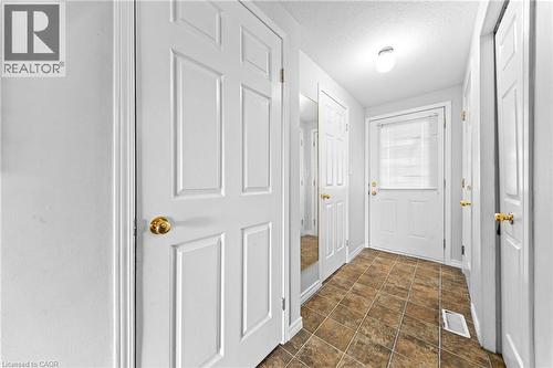 Entryway featuring durable tile flooring, a paneled door with an integrated window, bright overhead lighting, and multiple paneled interior doors with brass hardware - 245 Red Clover Court, Kitchener, ON 