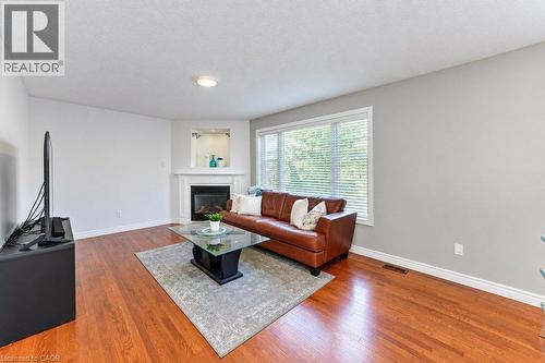 Hardwood flooring, corner fireplace with white mantel, recessed niche with accent lighting, large window with blinds, and flush mount ceiling light - 88 Decaro Crescent, Cambridge, ON 