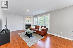 Hardwood flooring, corner fireplace with white mantel, recessed niche with accent lighting, large window with blinds, and flush mount ceiling light - 